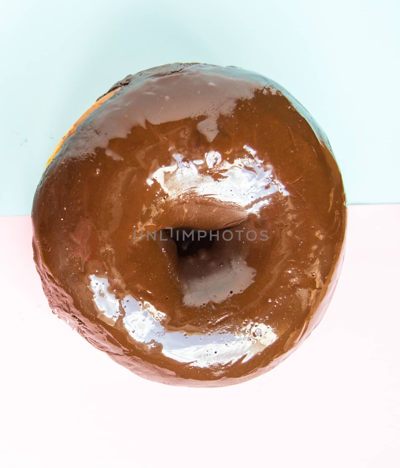 One chocolate donut on a light blue and pink background, top view.