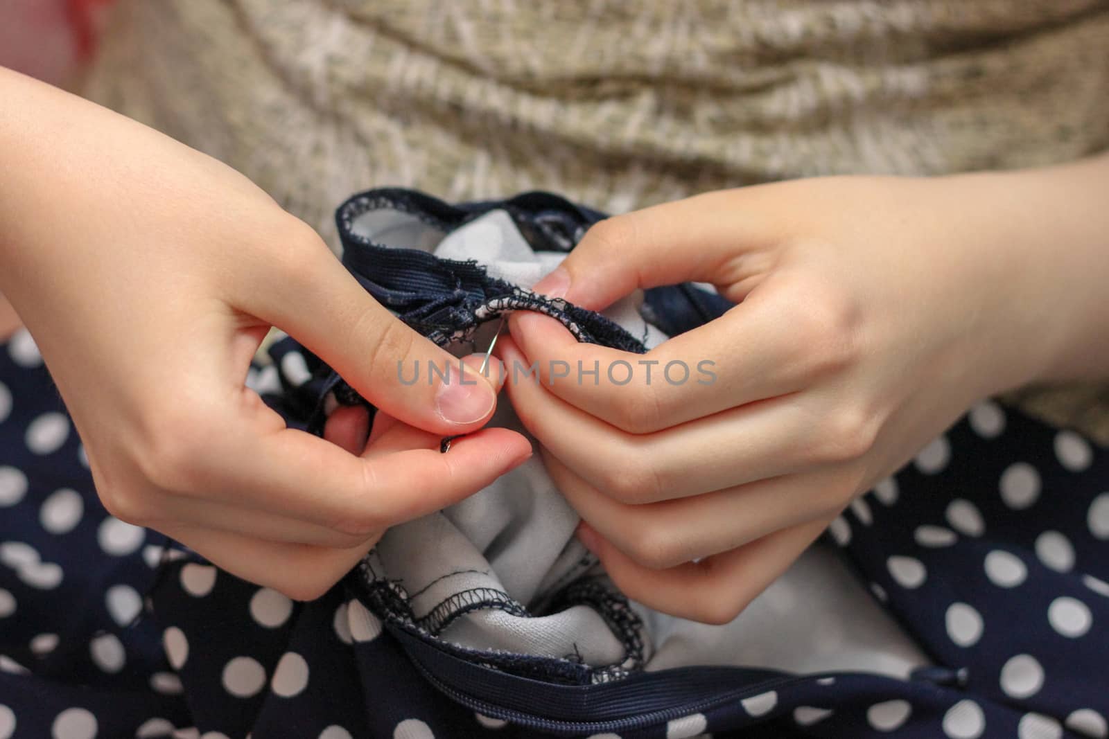 The girl sews with a needle. Needlework. Polka dot fabric