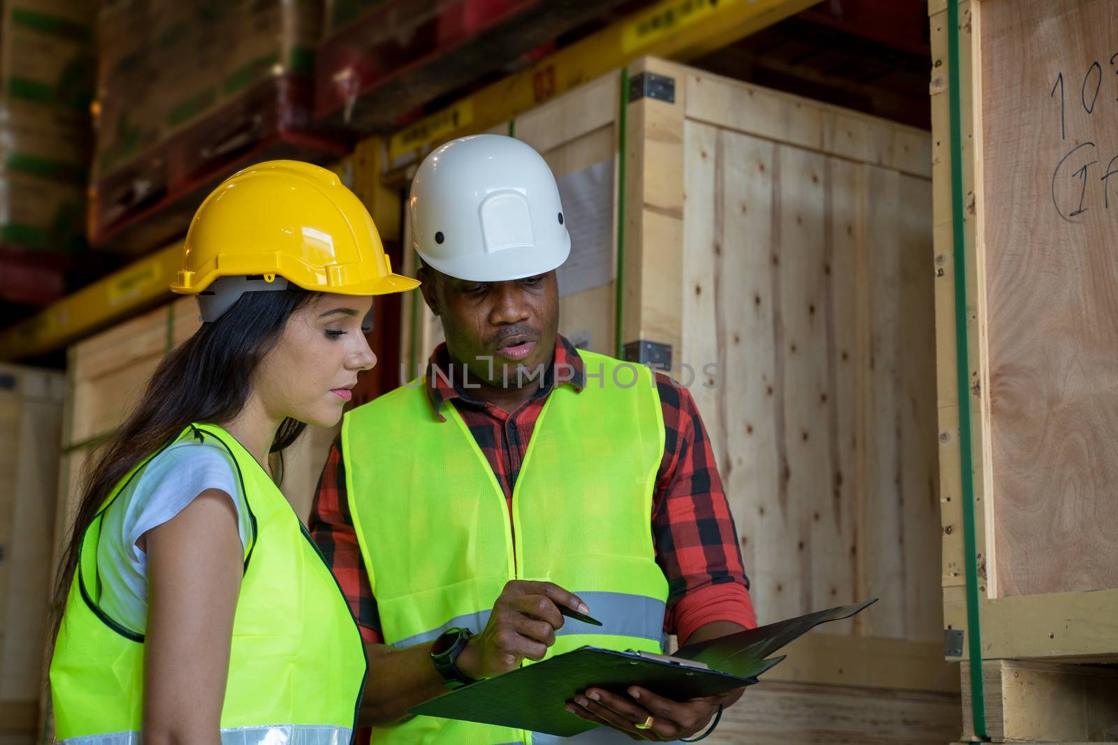 Warehouse manager and warehouse worker wearing helmet  with clipboard checking products about delivery schedule in industrial storage room.