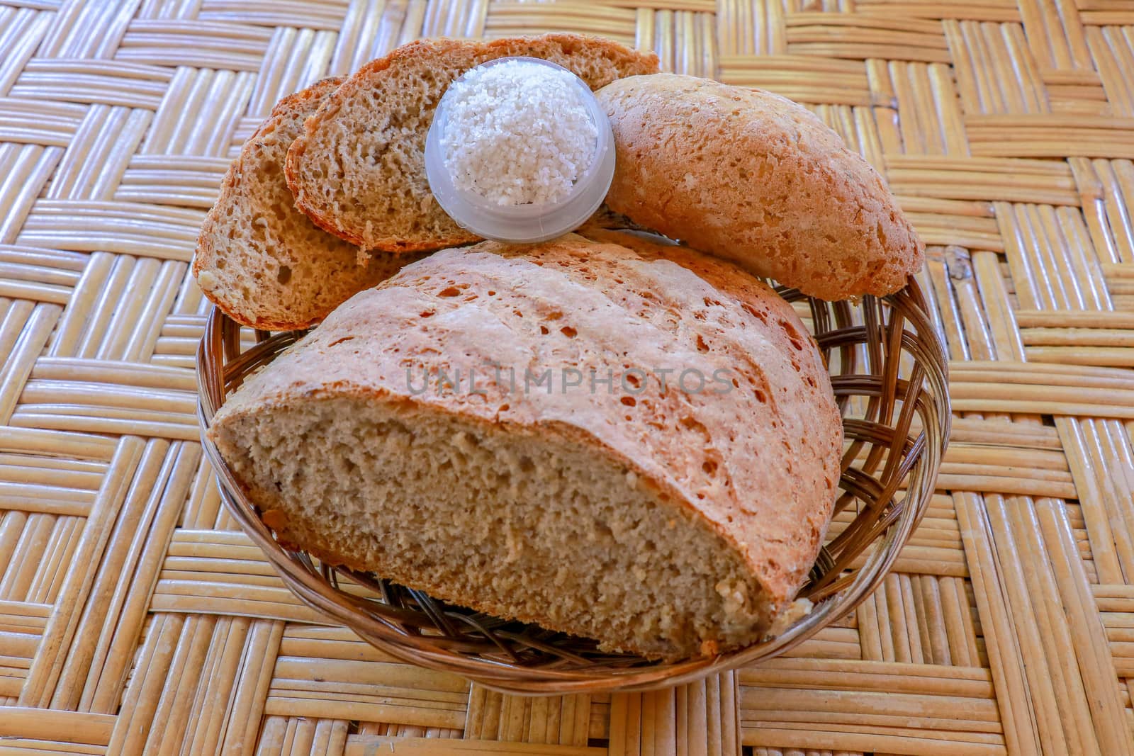 Fresh homemade bread made of wheat and rye flour. Sliced bread in a wicker basket. Bowl with salt. Delicious homemade pastries in a wicker basket. Healthy food on bamboo background.