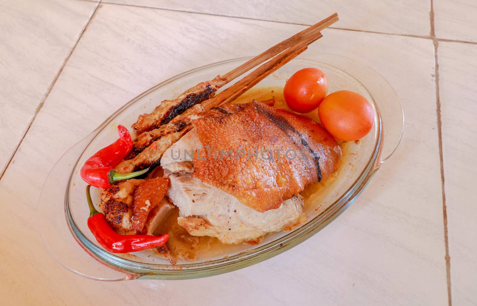 Roast pork in a glass roasting pan. Minced meat on a wooden stick. Crunchy and golden-baked skin. Hot chili peppers and fresh tomatoes. Glass baking.
