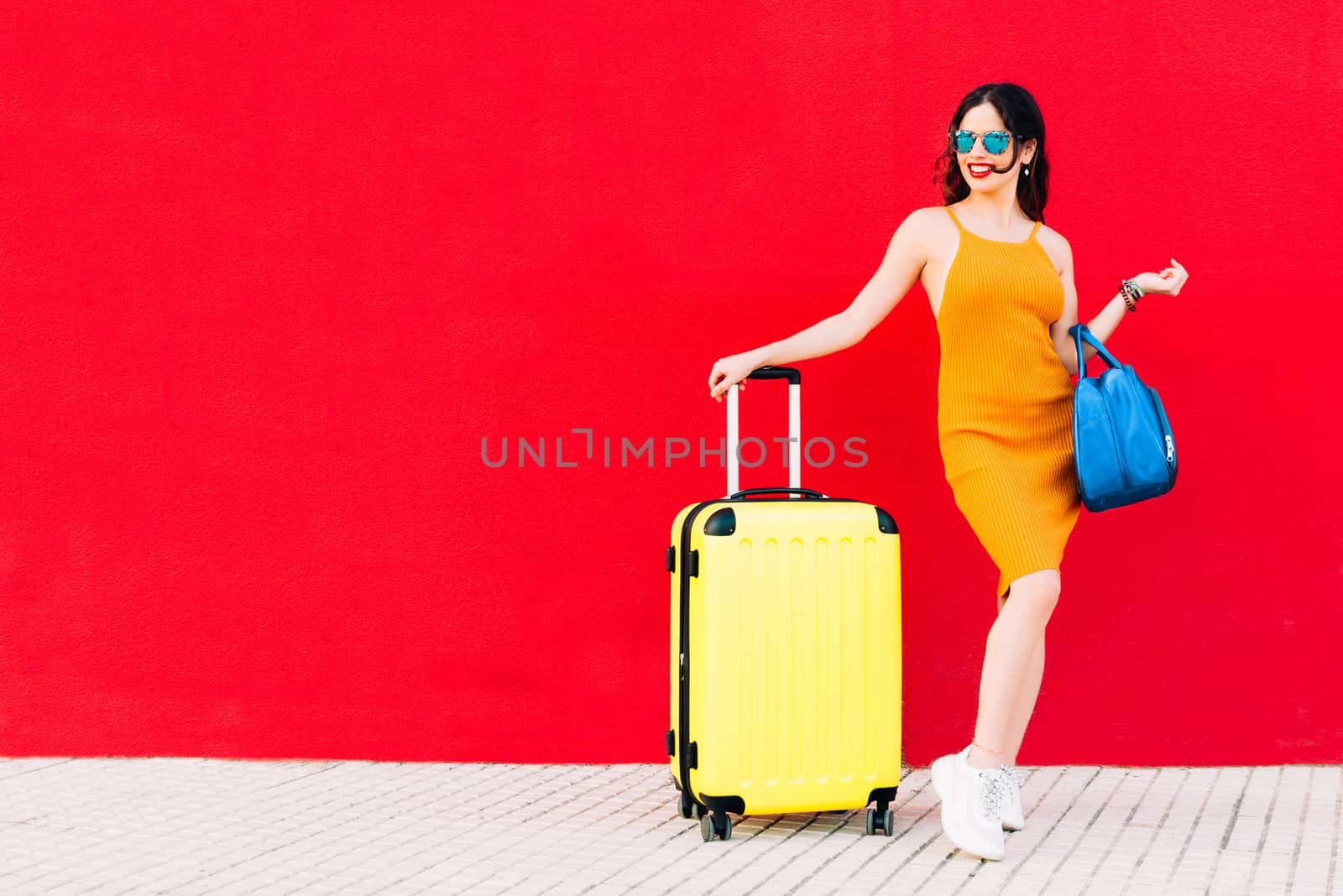 happy woman with sunglasses, yellow suitcase and blue handbag.