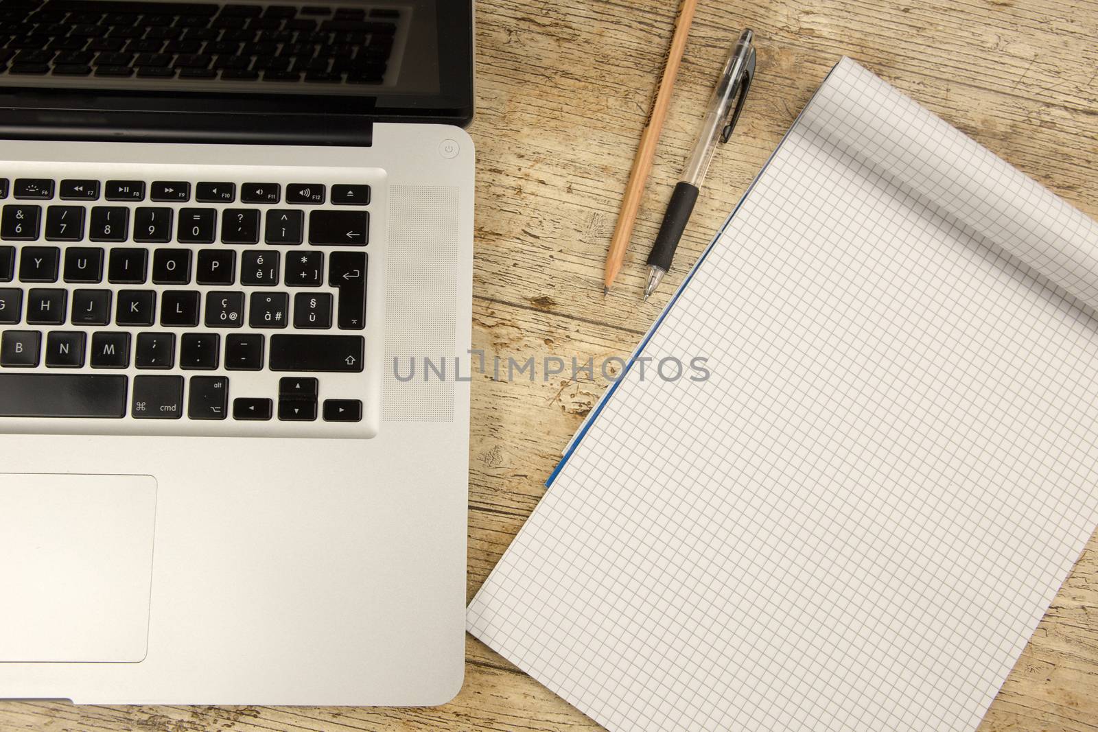 Contrast between old and new office work: shot from the top of an aluminum laptop on a wooden desk with an open checkered notebook, a pencil and a pen by robbyfontanesi