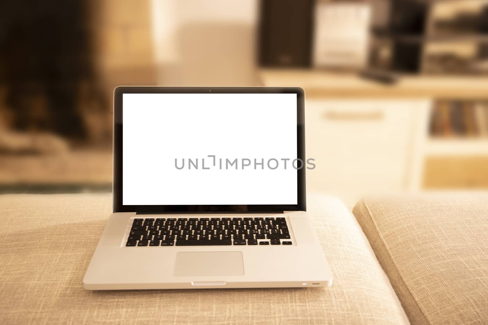 Open aluminum laptop with blank screen for copy space on a sofa ottoman in selective focus with shaded lounge background by robbyfontanesi