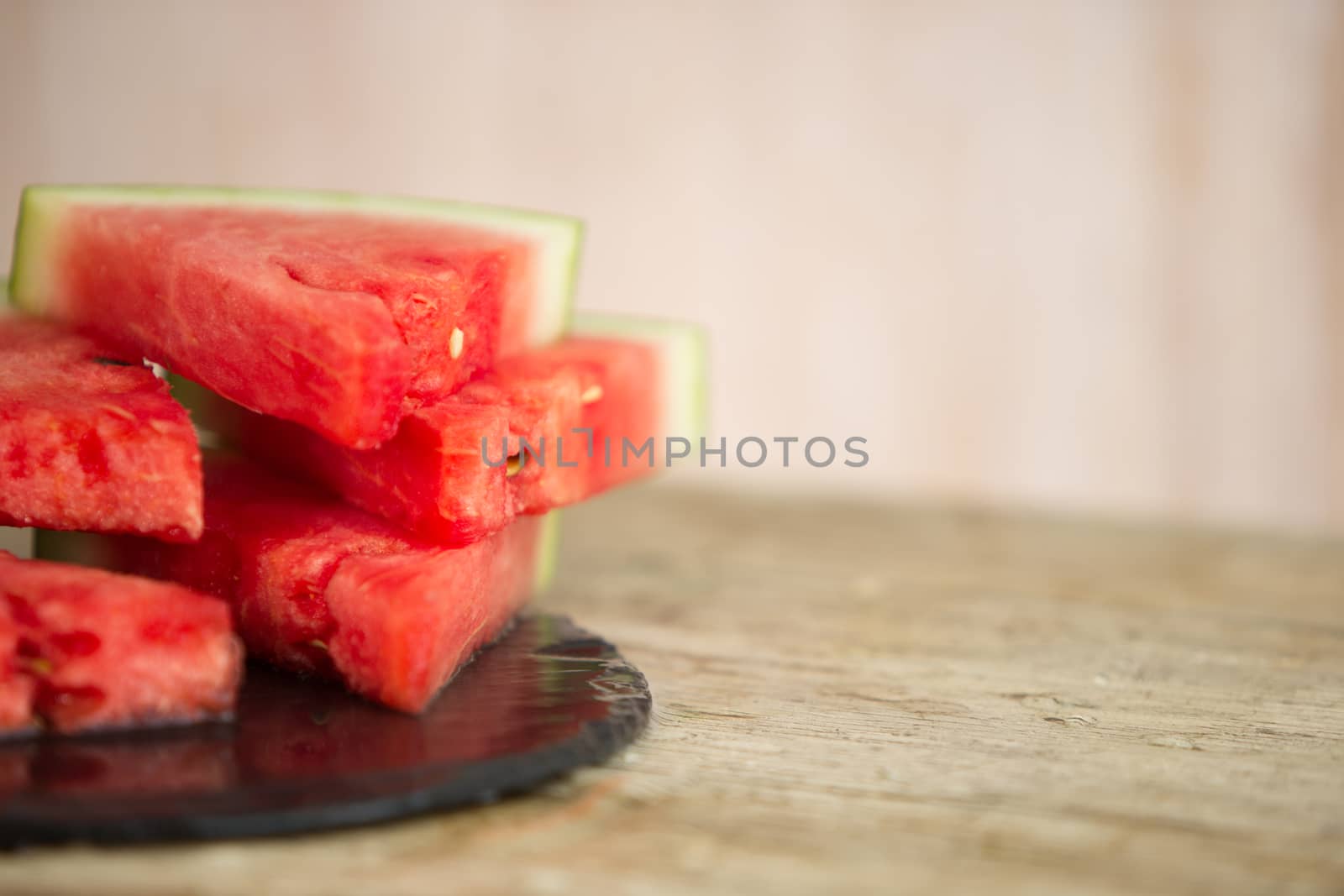 Triangular slices of watermelon overlaid on a black plate of wet slate in selective focus for copy space by robbyfontanesi