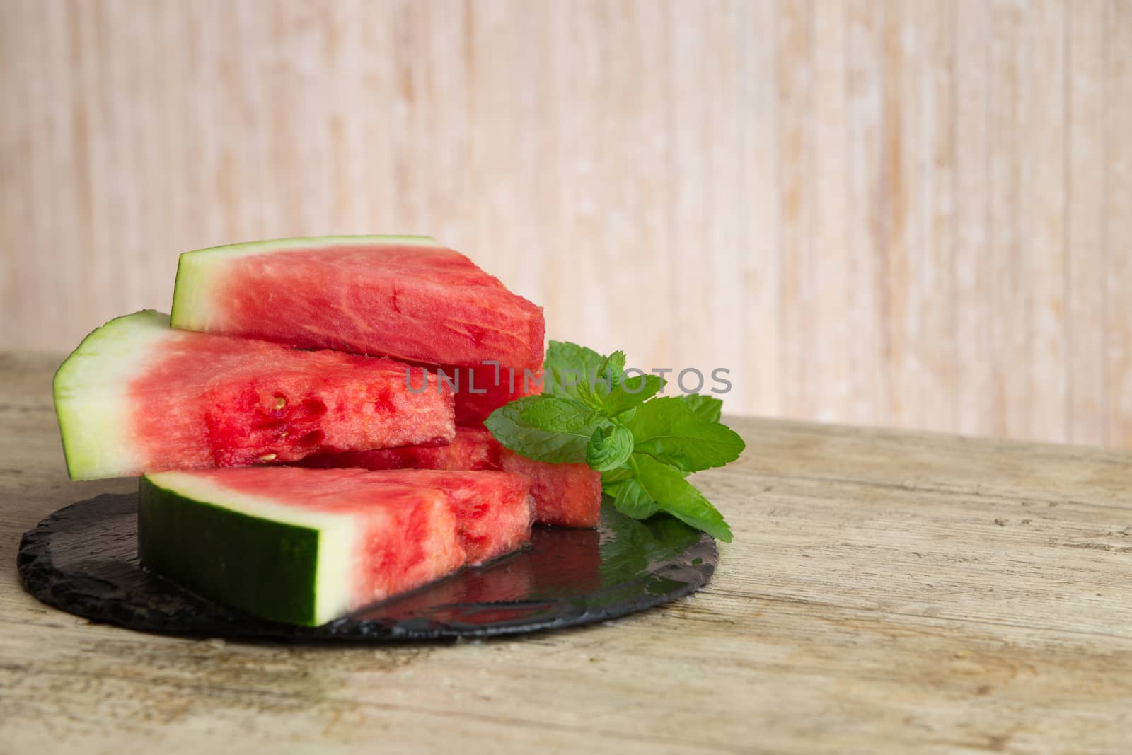 Triangular slices of watermelon overlaid on a black plate of wet slate with sprig of fresh green mint in selective focus for copy space