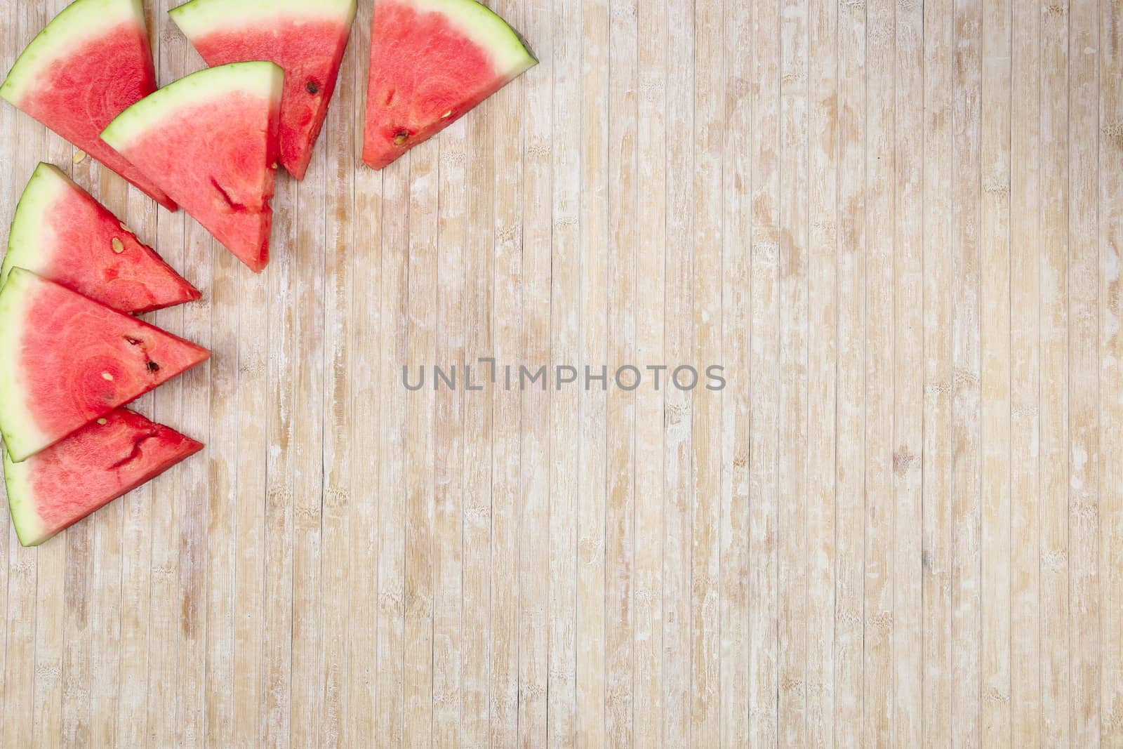 Triangular slices of watermelon that form geometric games for copy space on a light wooden background by robbyfontanesi