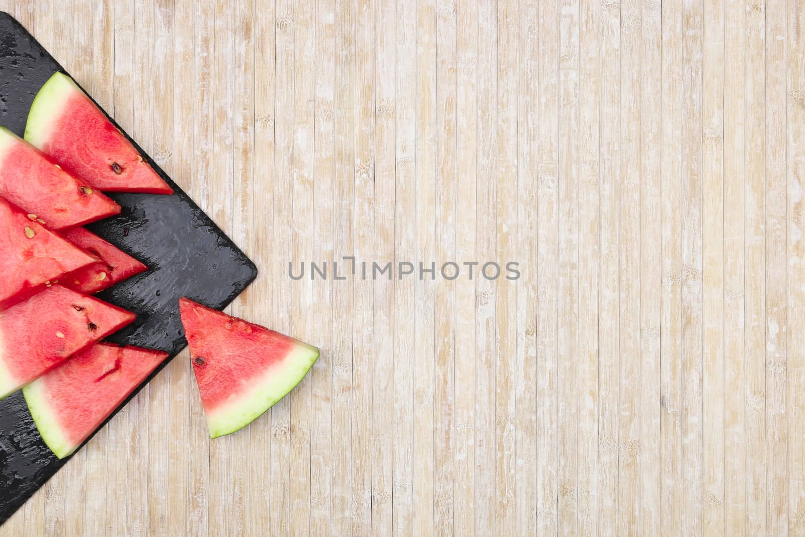 Triangular slices of watermelon on a black slate plate forming geometric games for copy space on a light wooden background by robbyfontanesi