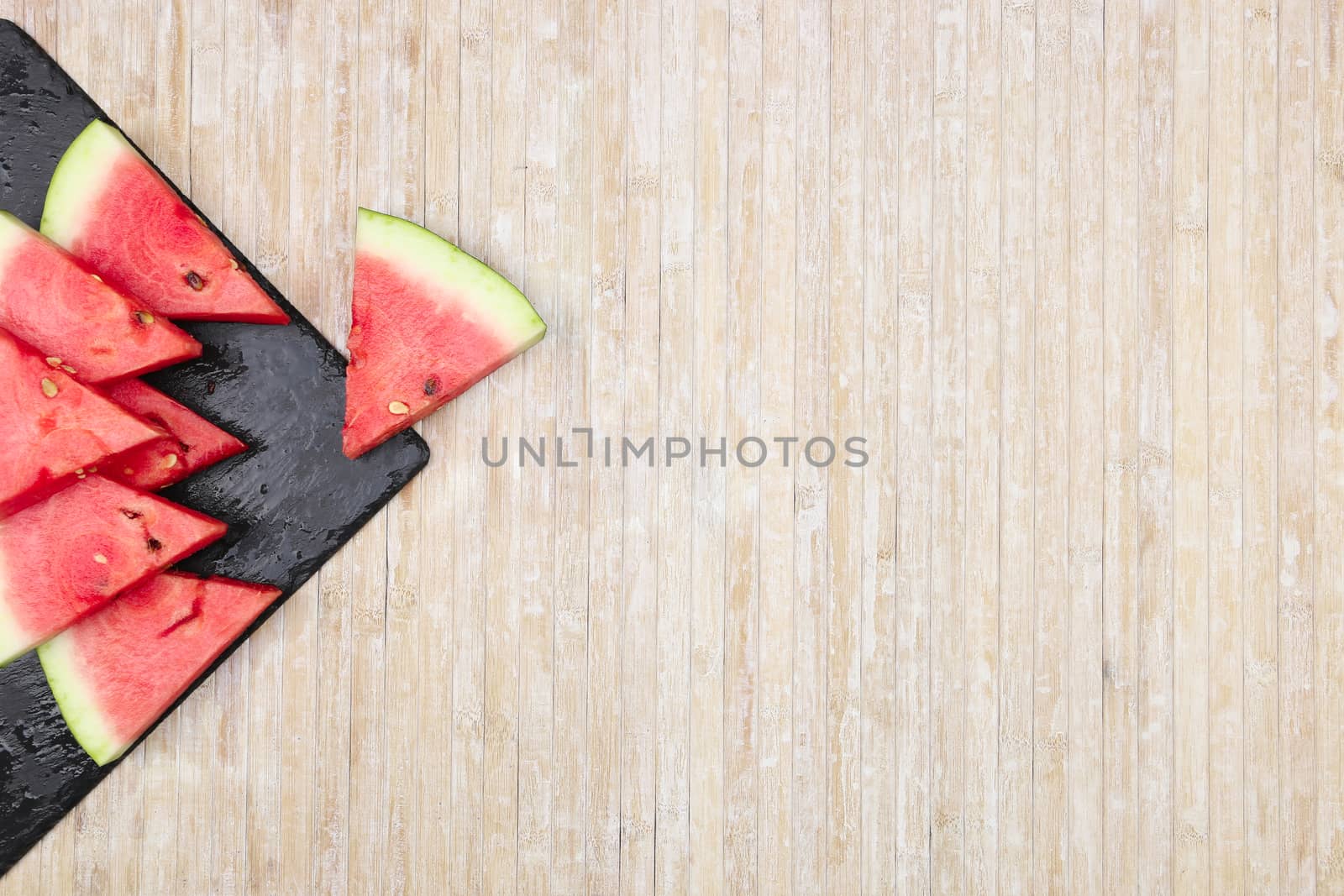 Triangular slices of watermelon on a black slate plate forming geometric games for copy space on a light wooden background