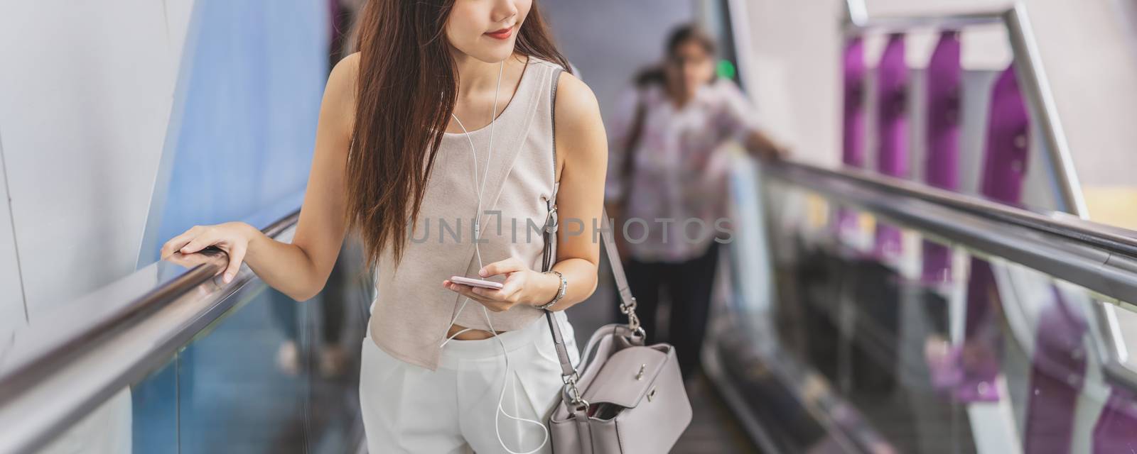 Banner, web page or cover template of Asian woman passenger using smart mobile phone and walking up escalator in subway station when traveling in big city, japanese, chinese, Korean lifestyle concept