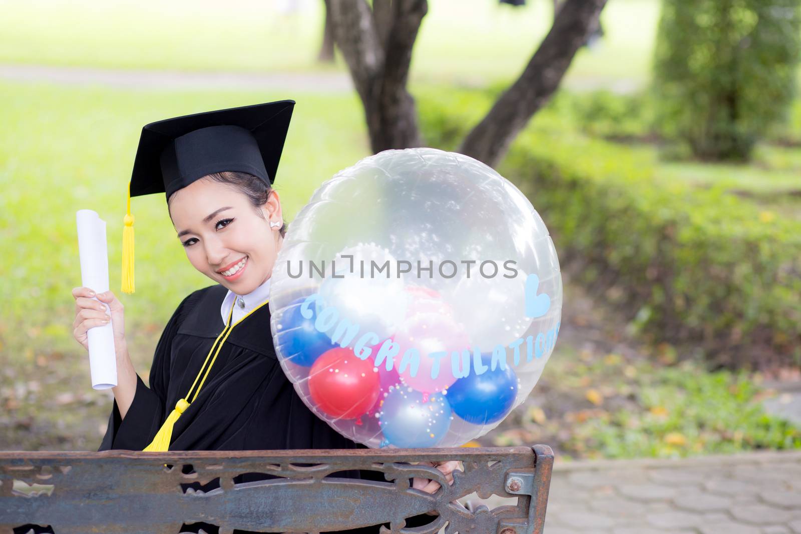 Portrait of happy young female graduates in academic dress and square academic cap holding word quotes of CONGRATS GRAD on balloon after convocation ceremony.