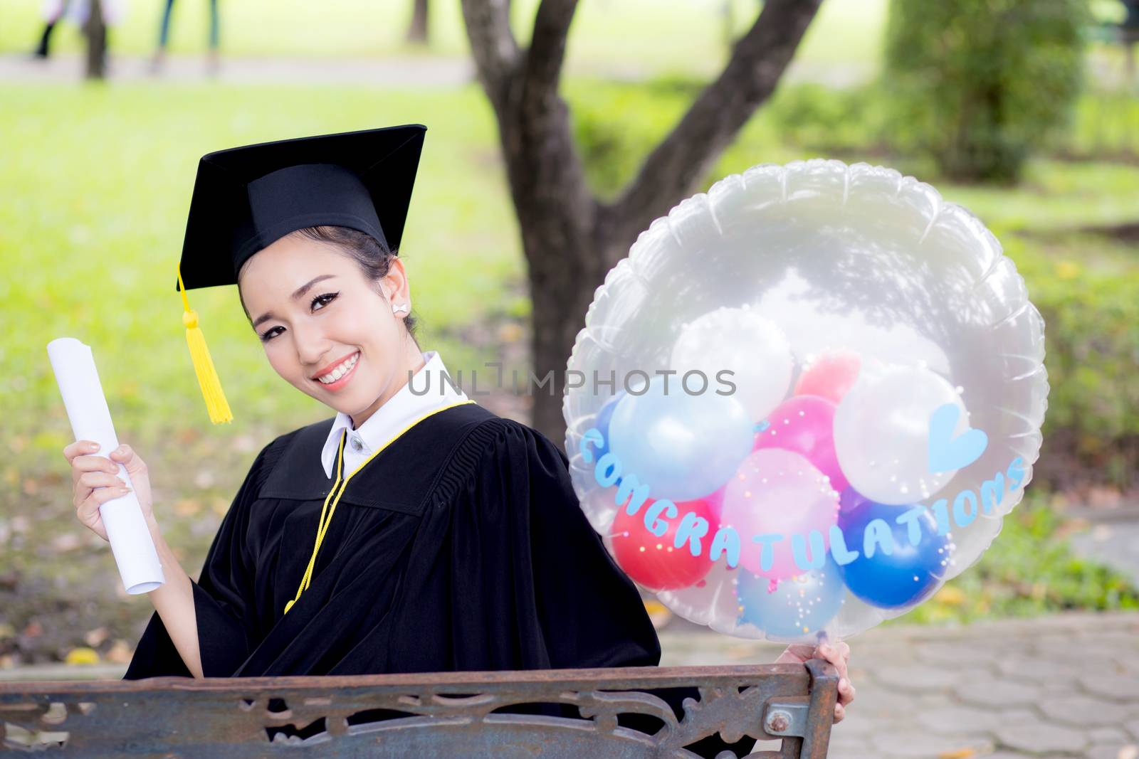 Portrait of happy young female graduates in academic dress and square academic cap holding word quotes of CONGRATS GRAD on balloon after convocation ceremony.