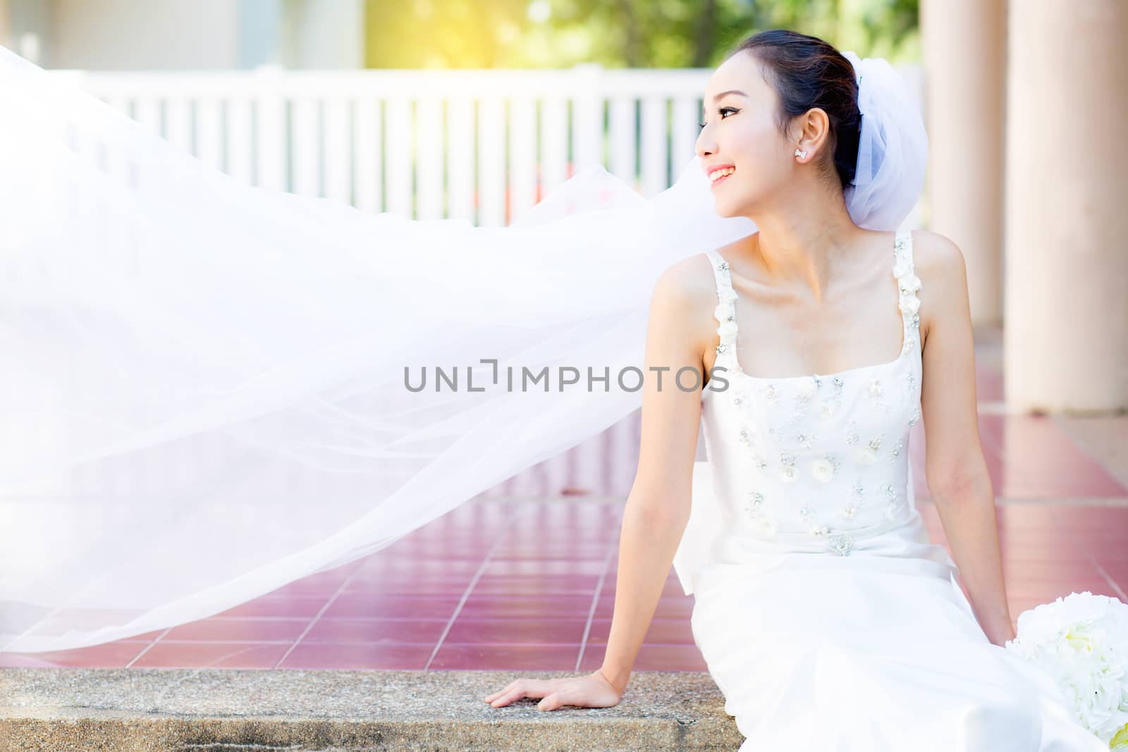 bride is sitting with flowers. Beautiful Young woman posing in park or garden in white bridal dress outdoors on a bright sunny day.