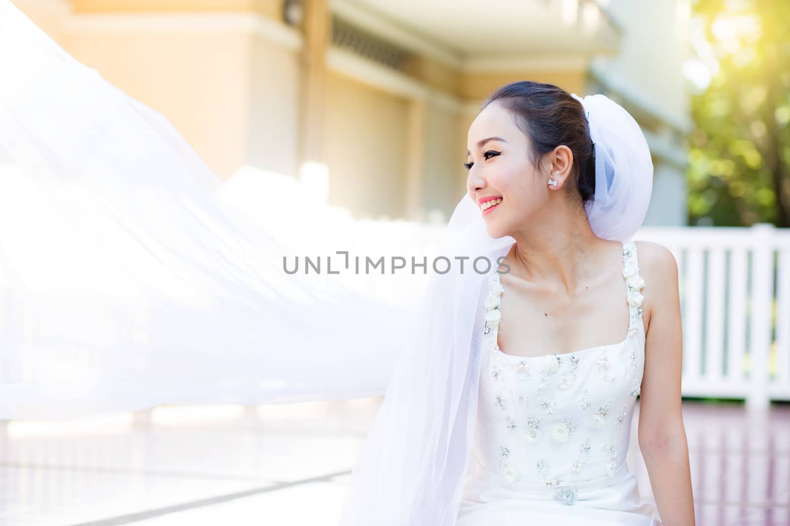 bride is sitting with flowers. Beautiful Young woman posing in park or garden in white bridal dress outdoors on a bright sunny day.