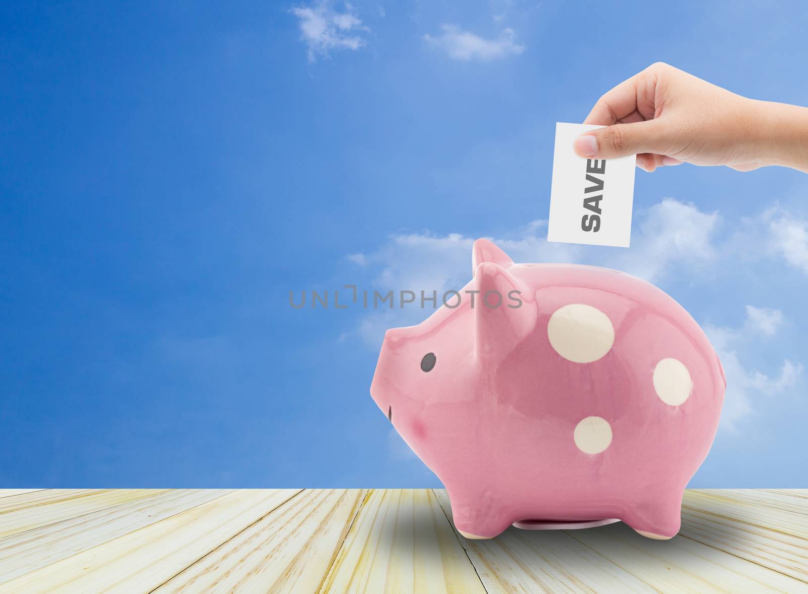 Close up view of the hand of a man placing a paper with save text into the slot of a piggy bank in a savings and investment concept