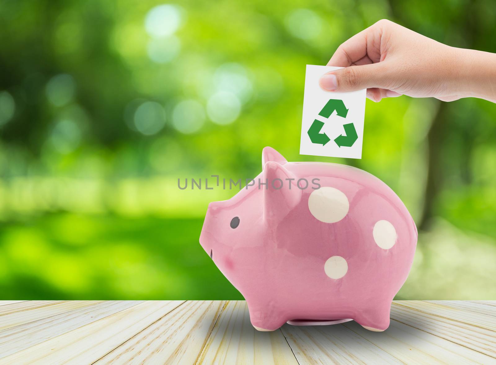 Close up view of the hand of a man placing a paper with symbol recycle into the slot of a piggy bank, environment concept
