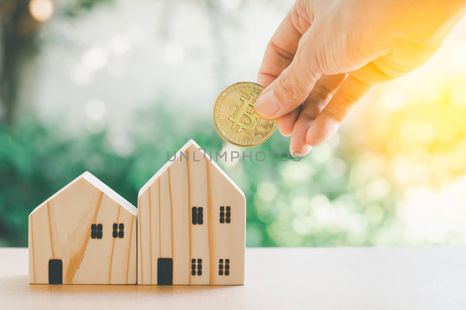 Saving money concept. Hand hold gloden coin with wooden model home on table with green bokeh background. Saving or investment for home in the future.