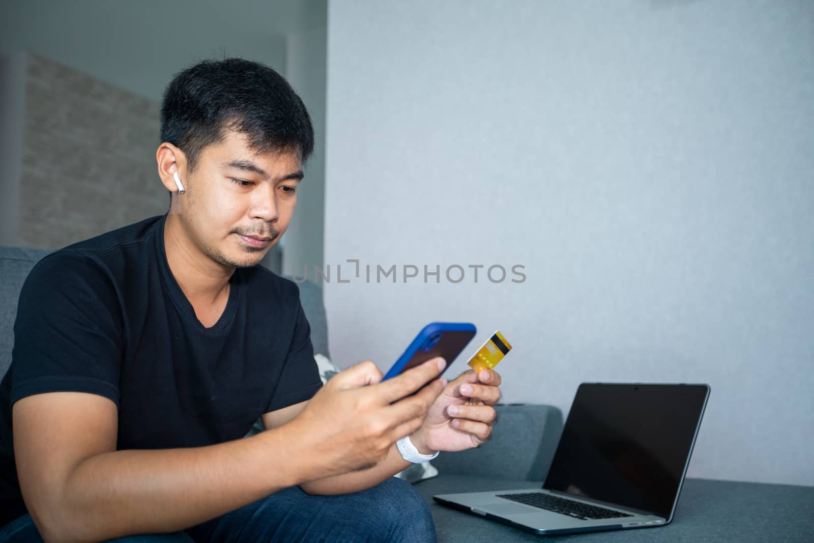 Asian man is holding credit card and using smart phone shopping online at home.Online shopping, e-commerce, internet banking, spending money, working from home concept