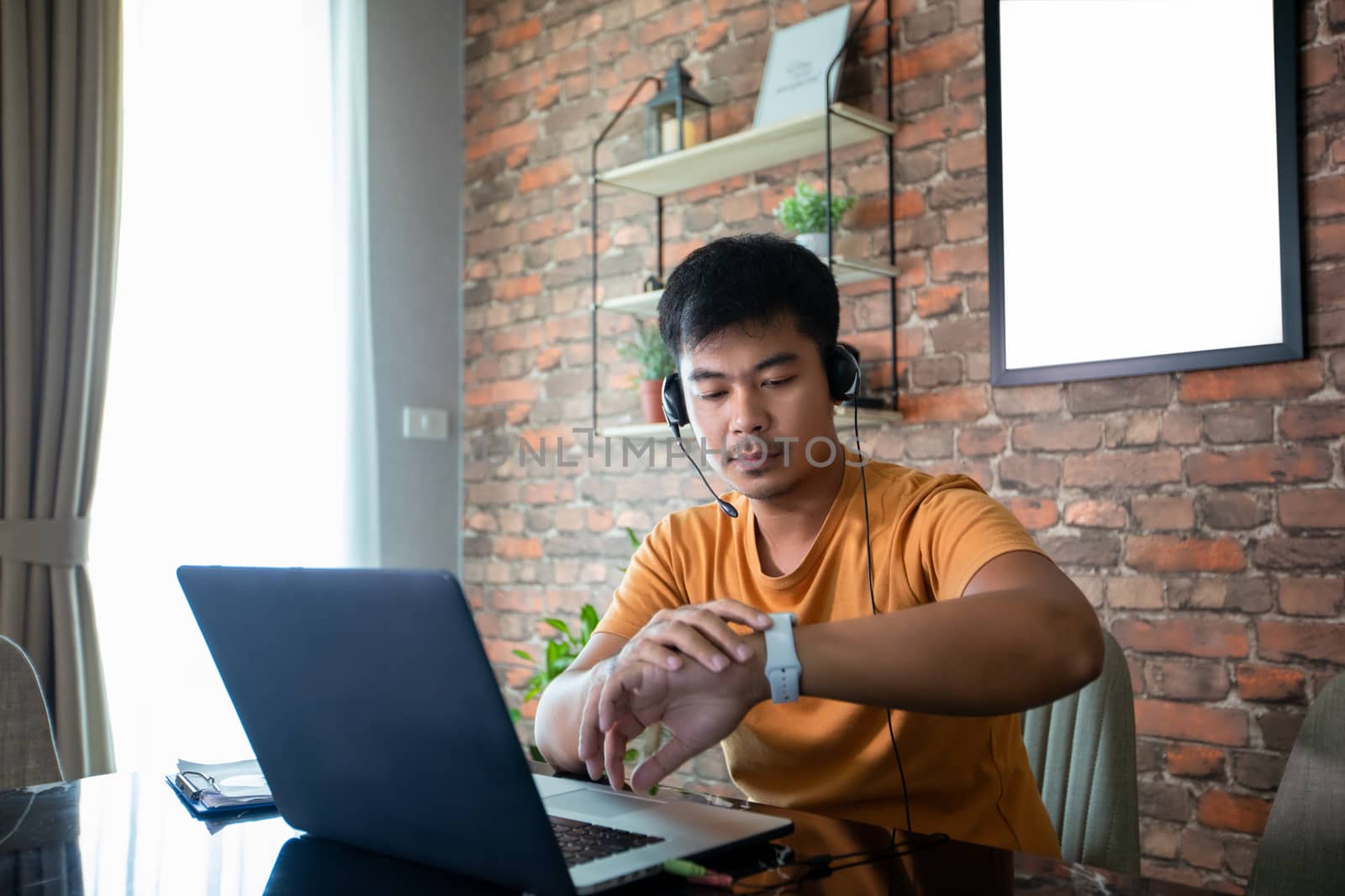 Asian man is watching the time and he uses a notebook computer to work at home. by Tuiphotoengineer