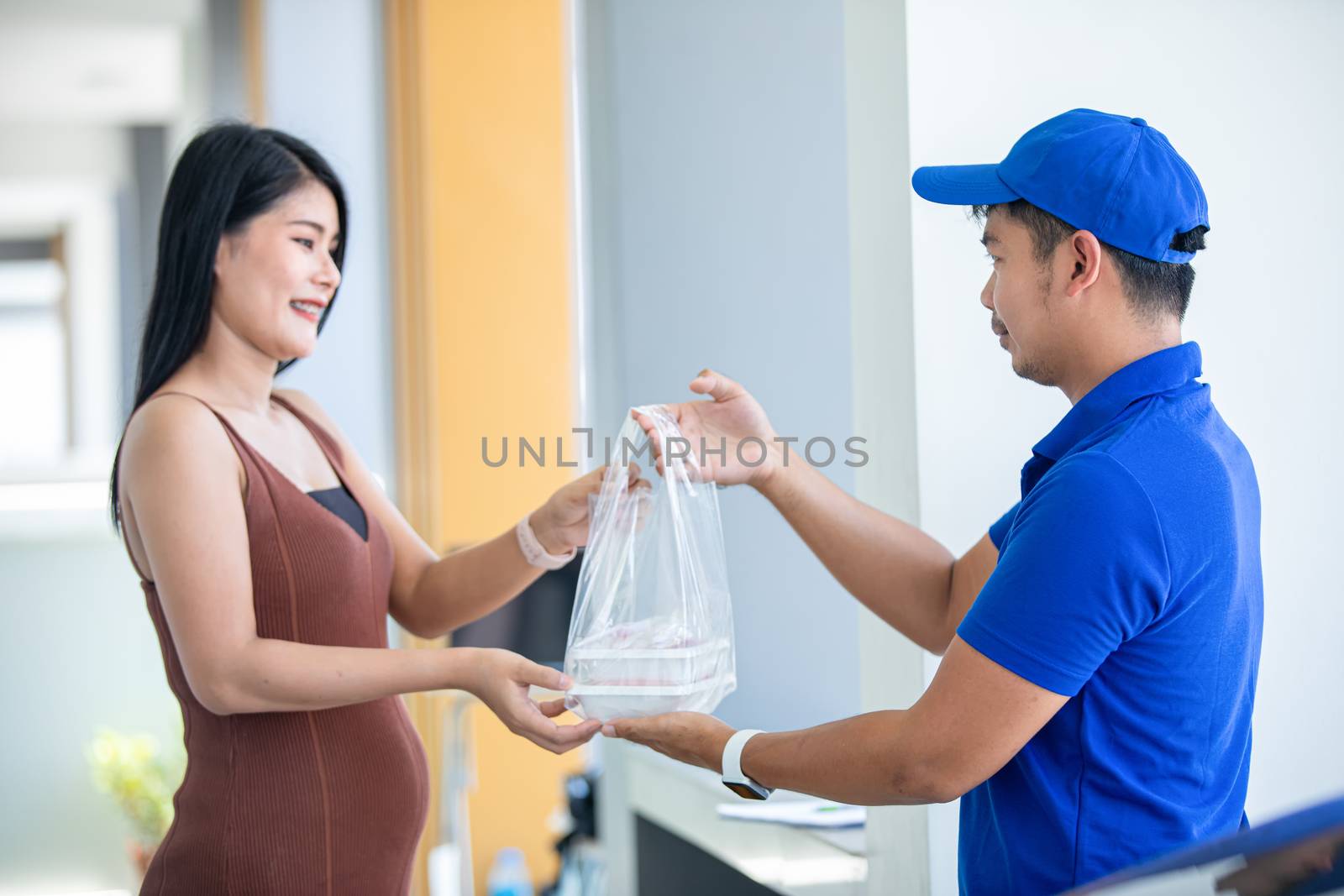 Asian delivery servicemen wearing a blue uniform with a blue cap and handling food boxes in plastic bags to give to the customer in front of the house. Online shopping and Express delivery