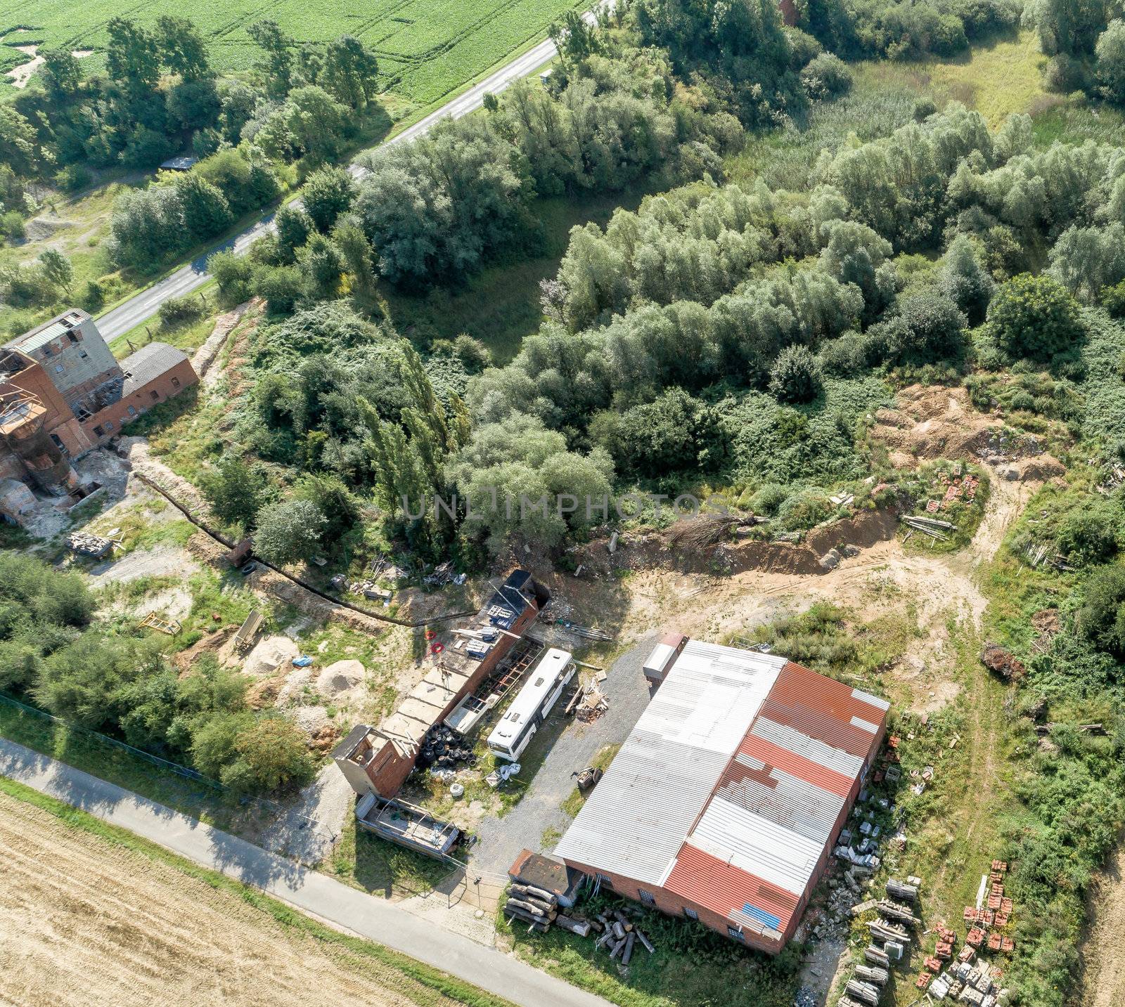 Downsized plant for the repair of machines with a scrap yard behind a forest with a wild dump, diagonally shot aerial photograph. by geogif