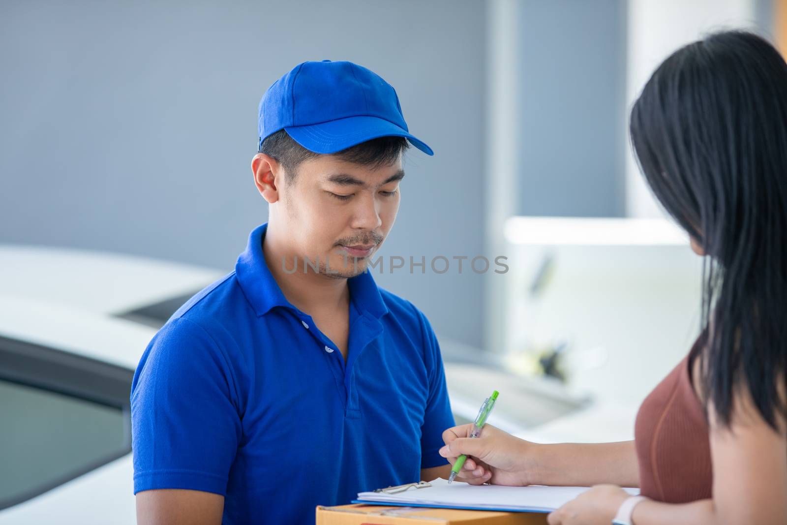 Asian delivery servicemen wearing a blue uniform with a bluecap and  handling cardboard boxes to give to the female customer in front of the house. Online shopping and Express delivery by Tuiphotoengineer