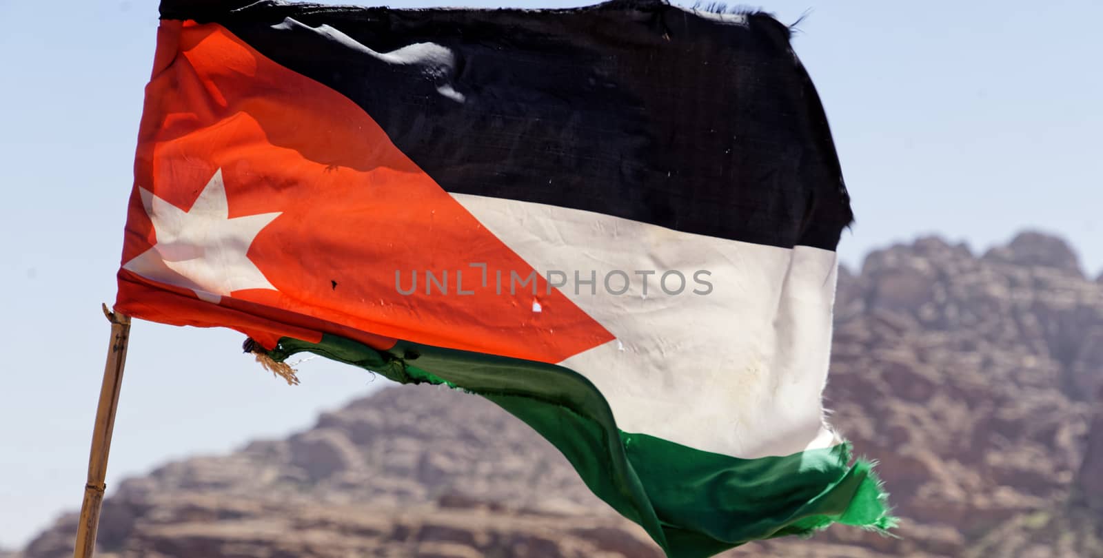 Slightly battered flag of the land Jordan on the high windy cliffs of Petra, Wadi Musa, Jordan, by geogif