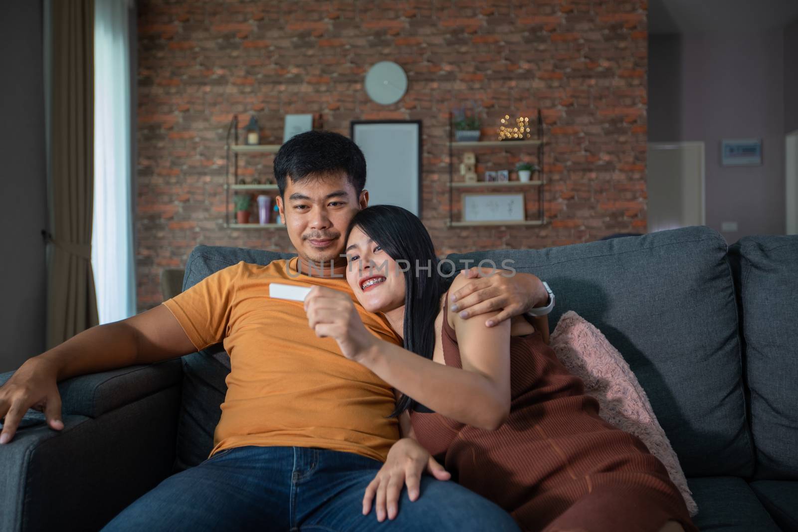Happy Asian couple smiling looking cheerful after a home pregnancy test in sofa at home by Tuiphotoengineer