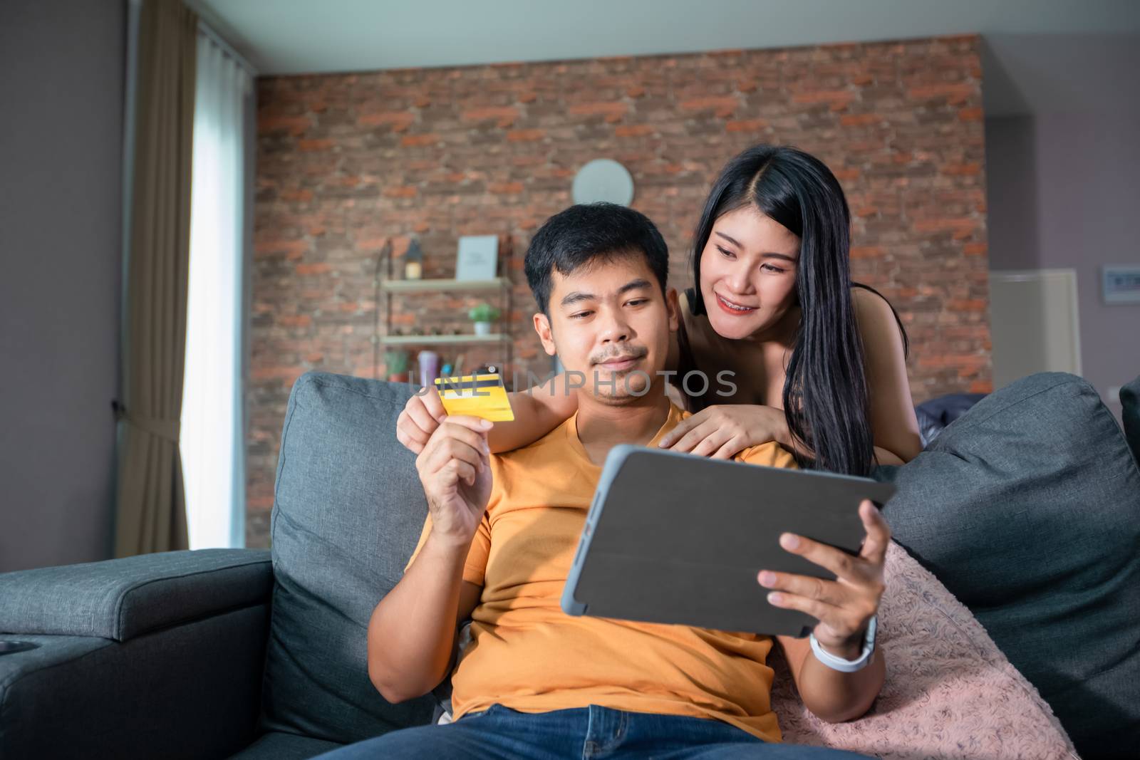 Asian Couple shopping online and paying with credit card at laptop computer,Happy couple at home surfing the net on sofa by Tuiphotoengineer