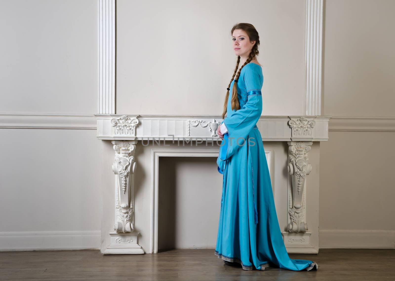 Pretty young woman in historical medieval blue dress poses in studio