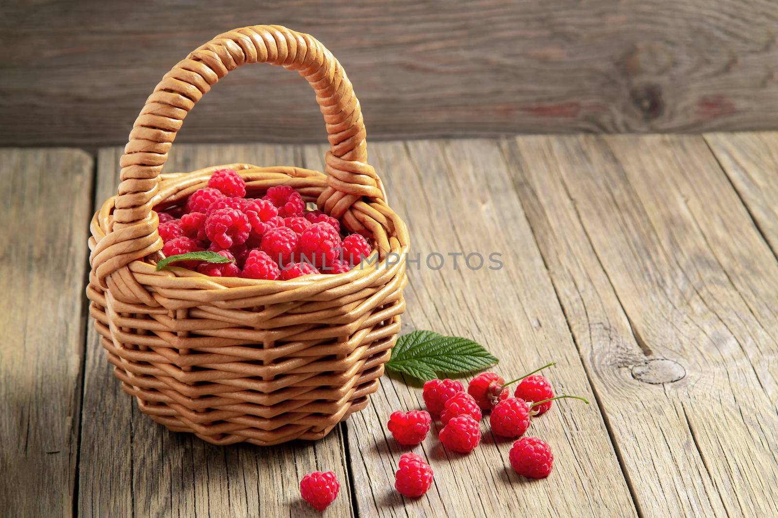 Ripe forest raspberries in a small basket on a wooden table, copy space by galsand