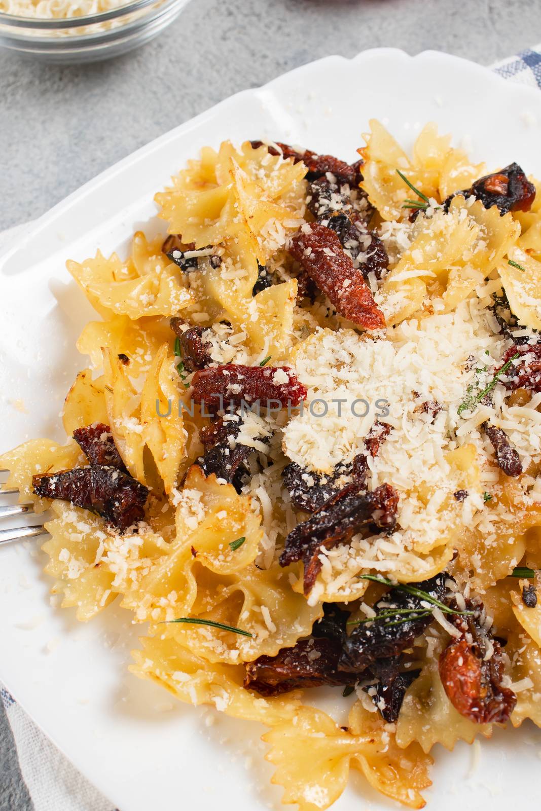 Pasta with sun dried tomatoes and parmesan in a white plate on the table. Italian food dish, vertical image.