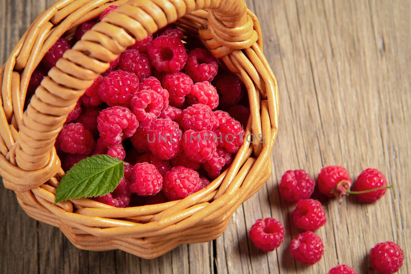 Ripe forest raspberries in a small basket on a wooden table, top view.