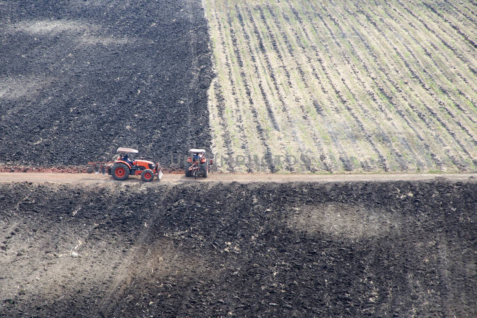 Two tractors working on burned farmland.