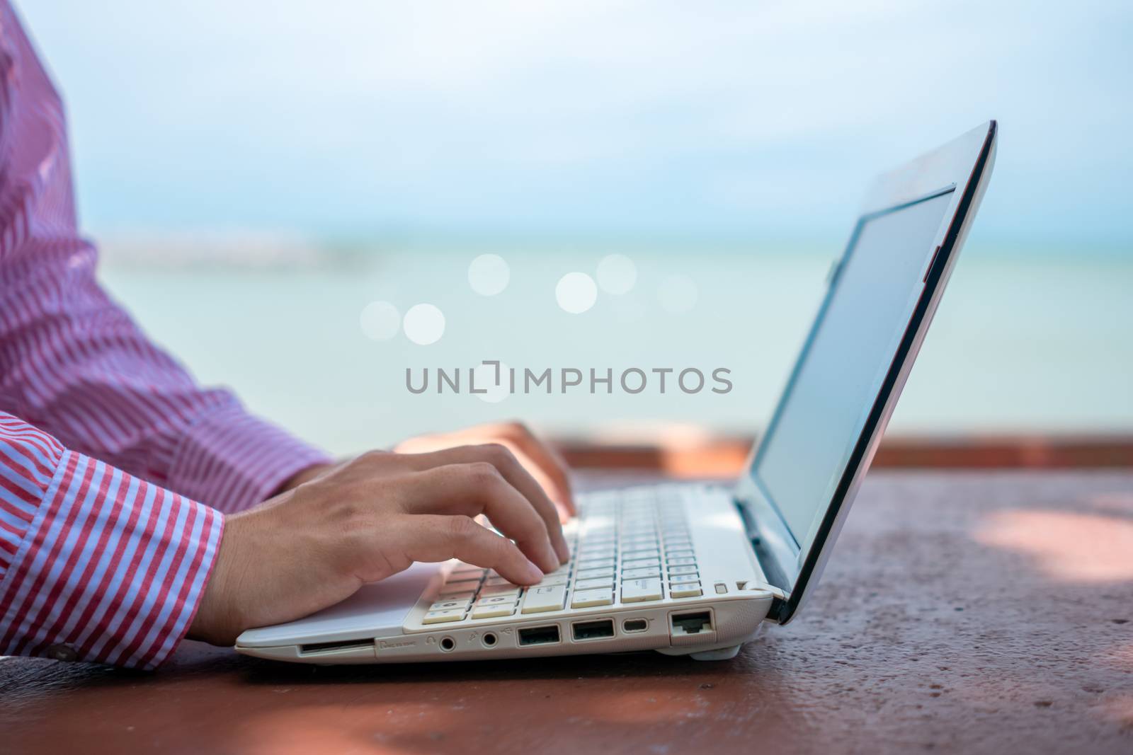 Woman hand using laptop to work study on work desk with clean nature beach outdoor background. Business, financial concept. by Suwant