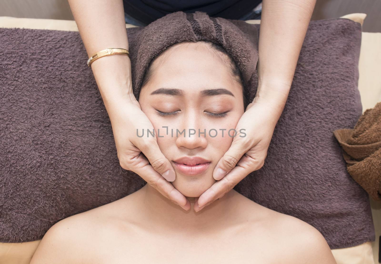  young asian woman with closed eyes getting a massage on her face in spa treatment