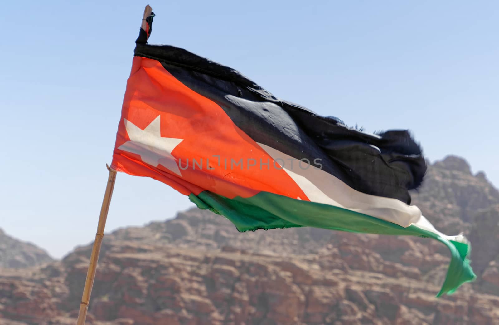 Slightly battered flag of the land Jordan on the high windy cliffs of Petra, Wadi Musa, Jordan, middle east