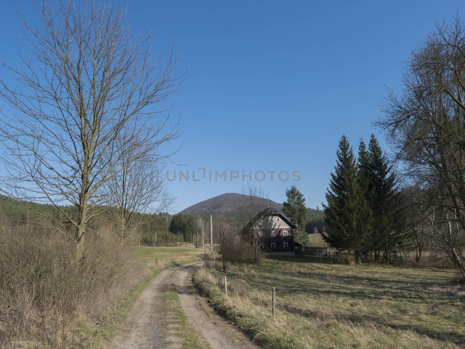 country road with old rustic cottage half timbered house in solitude near village Marenicky in luzicke hory, Lusatian Mountains, early spring, blue sky.