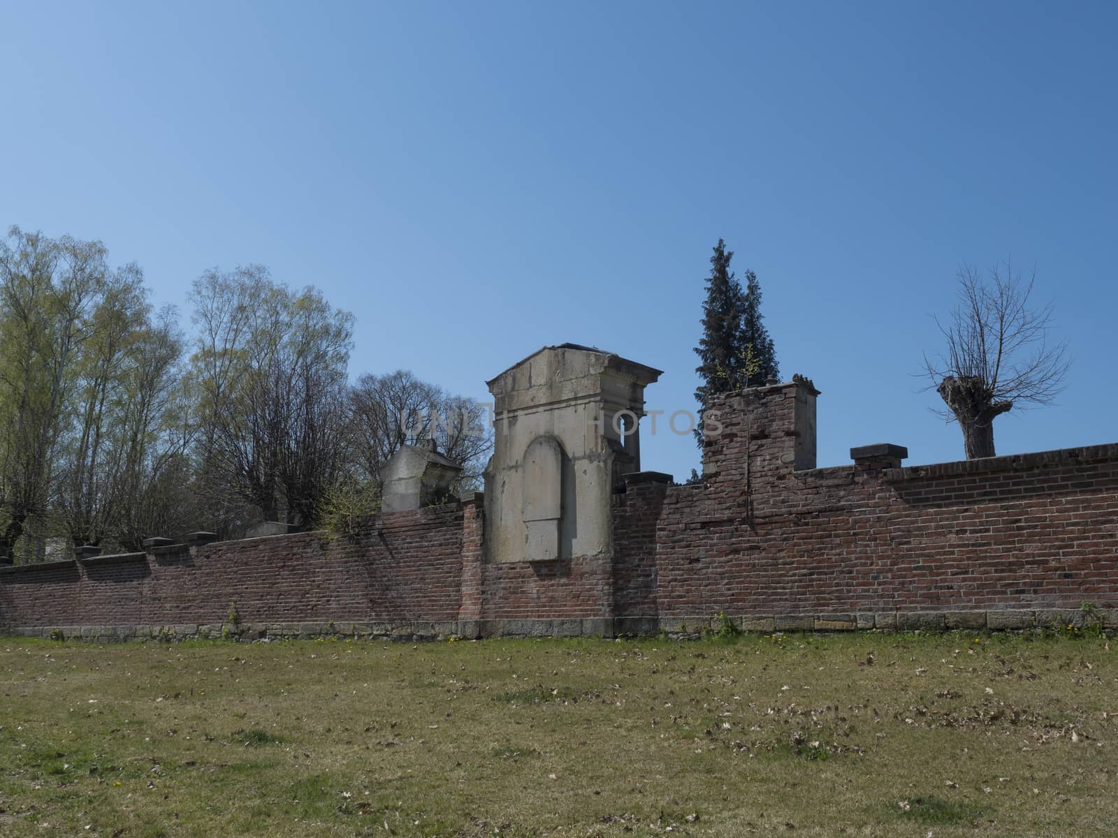 old red brick wall of country cemetery at village Cvikov in luzicke hory, Lusatian Mountains, early spring, blue sky by Henkeova