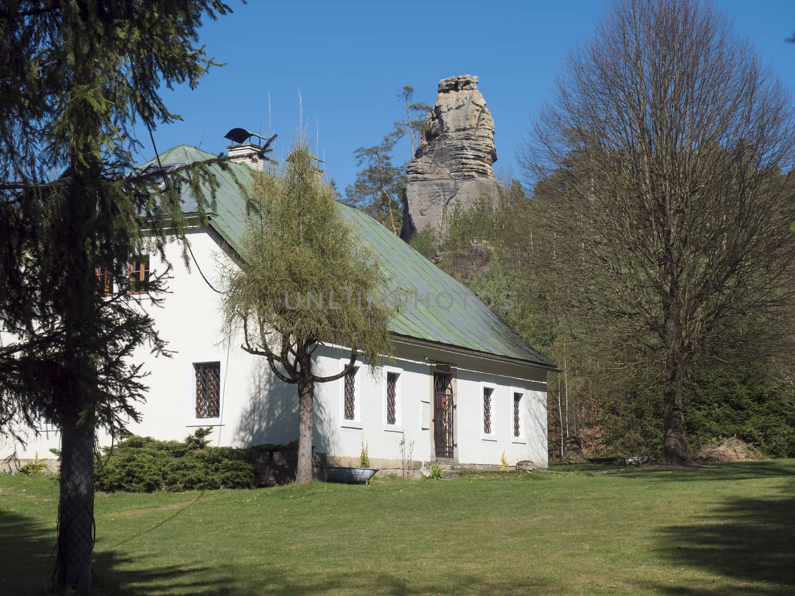 Country house, old rustic cottage with sandstone rock pillar in spring landscape at Lusatian Mountains with spring green grass and trees, Blue sky background.