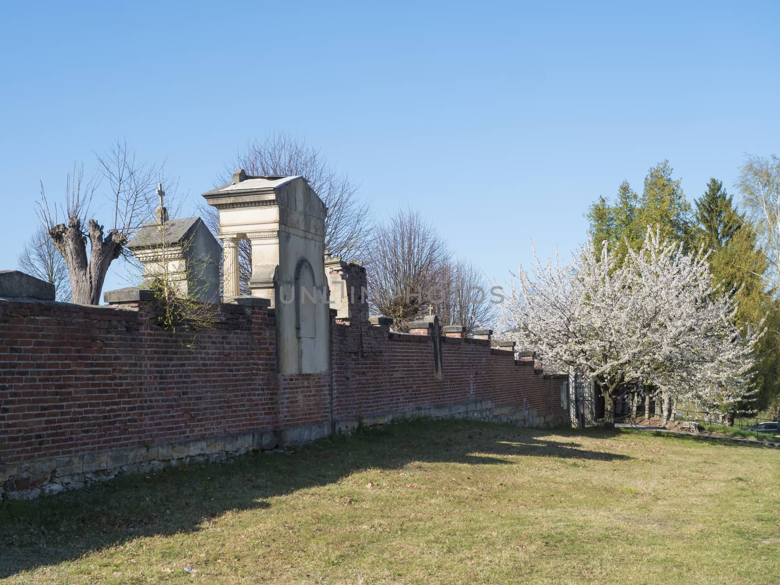 old red brick wall of country cemetery at village Cvikov in luzicke hory, Lusatian Mountains, early spring, blue sky.