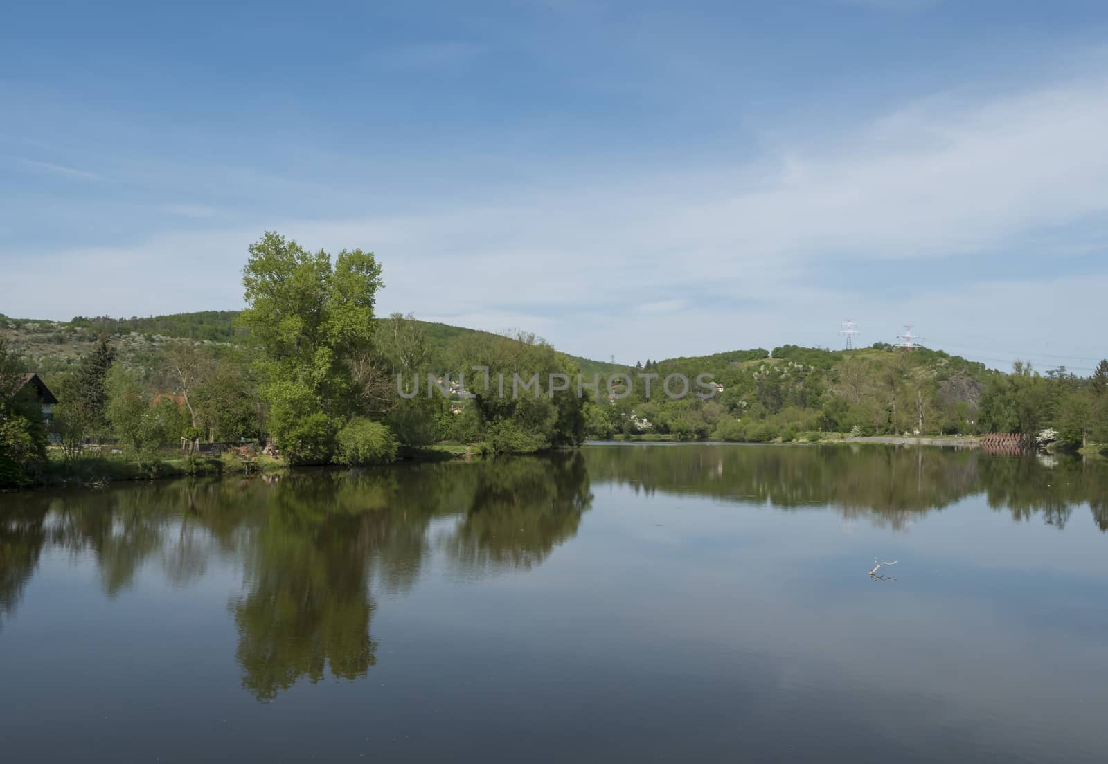 view on river Berounka from pedestrial bridge from village Zadni Treban to Hlasna treban in central Bohemian region, green lush trees reflecting in water, blue sky, spring sunny day by Henkeova