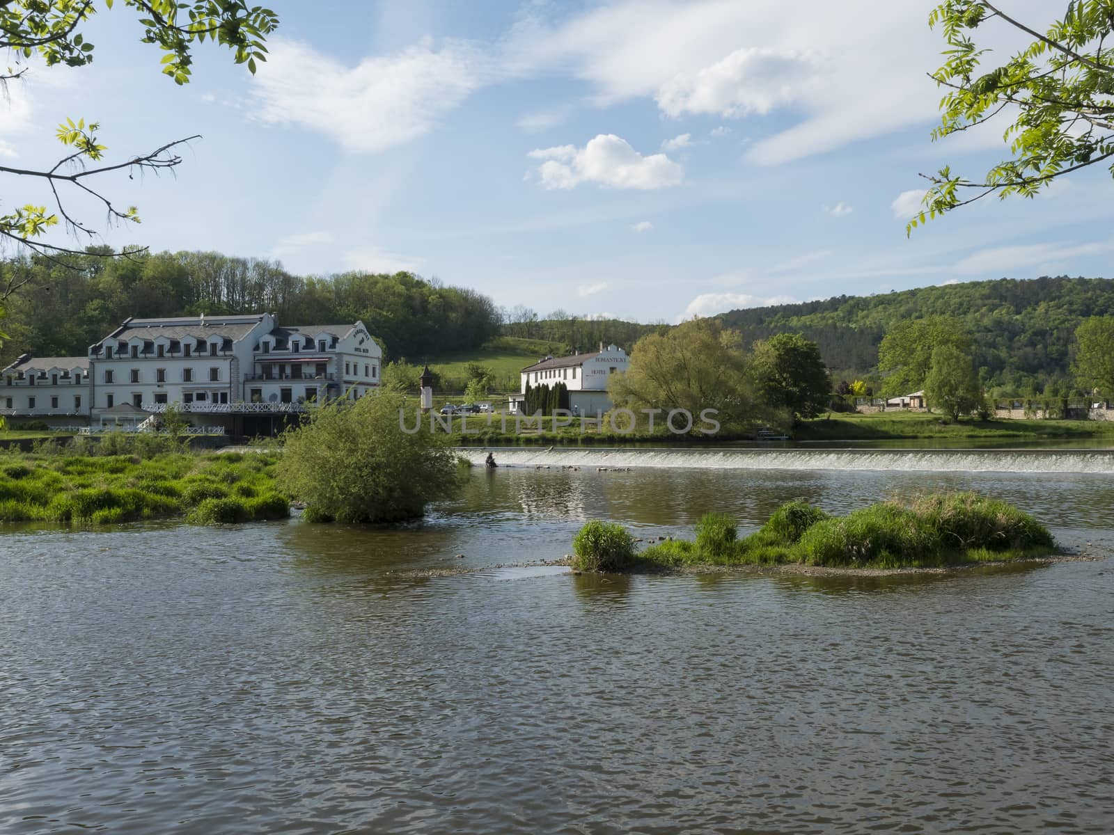 View on the river Berounka in village Zadni Treban with weir and building of Hotel Mlyn Karlstejn, sunny summer day, Czech Rupublic.