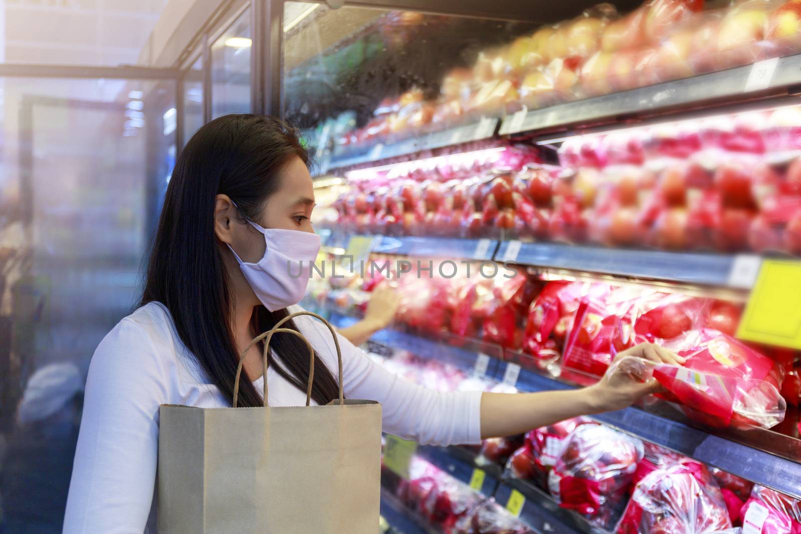 Asian woman wearing protective face mask hold paper shopping bag in supermarket department store. Girl, looking grocery to buy  some fruit. New normal after covid-19. Family concept.