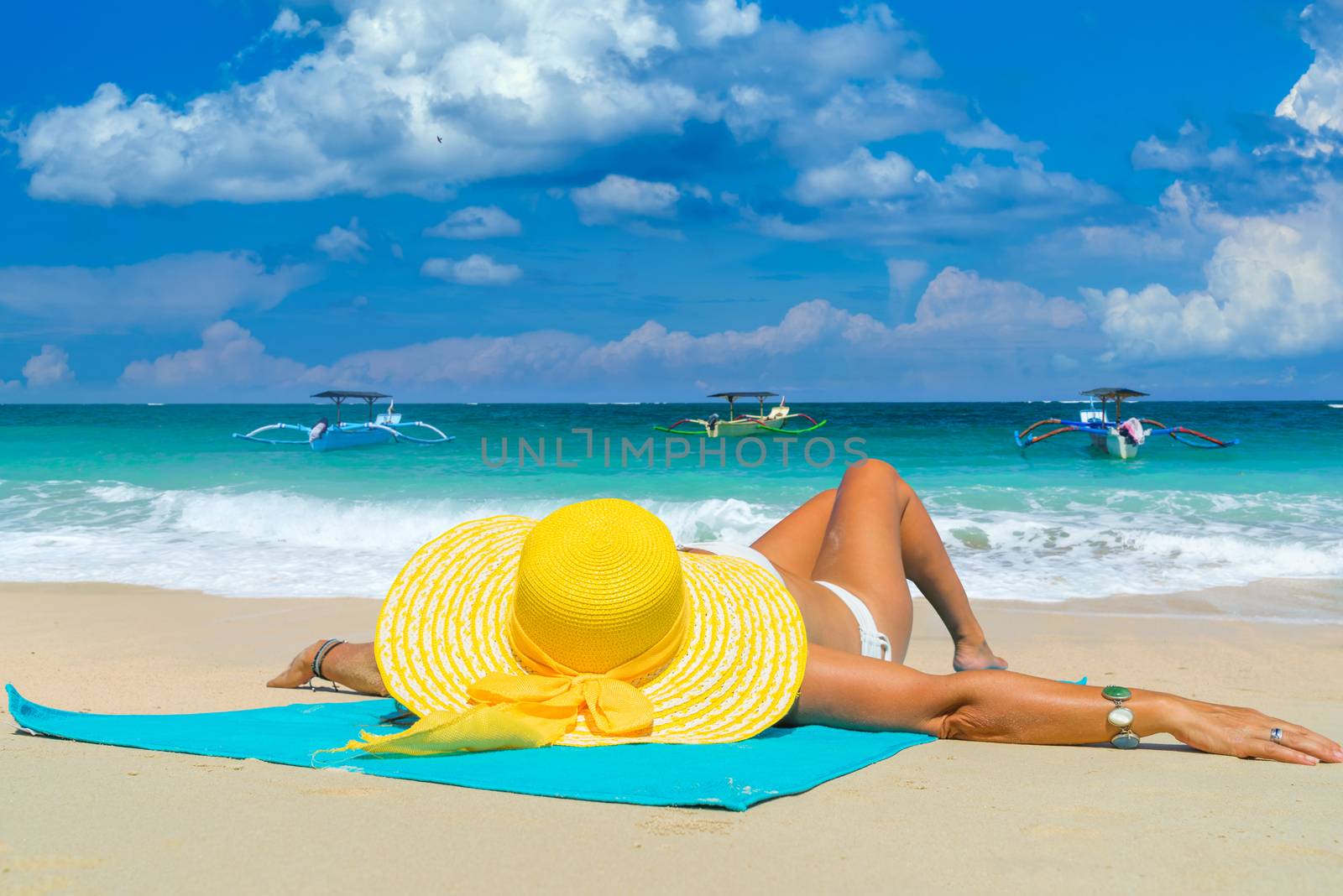 Woman in yellow bikini lying on tropical beach in Bali 