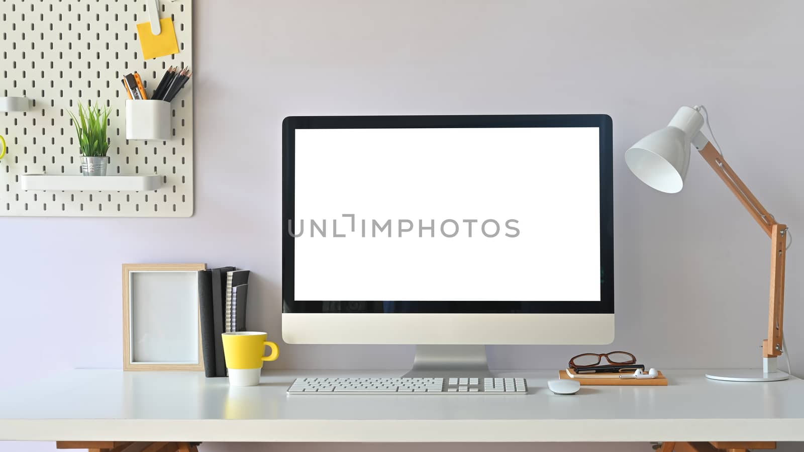 Workspace computer mockup and office supplies with peg board on wooden table.