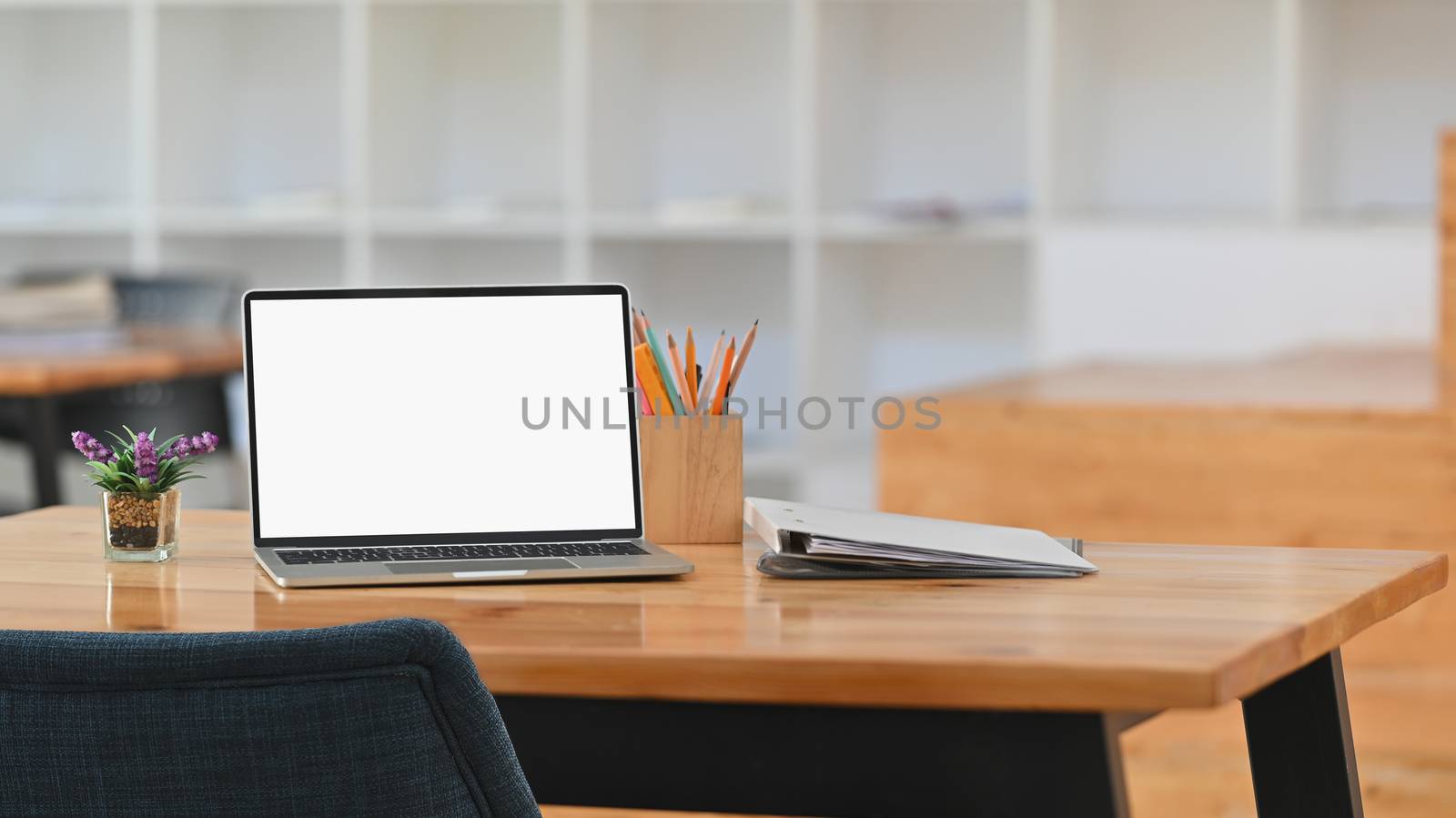 Front of white blank screen laptop, pencil holder, document files, potted plant on a working desk.