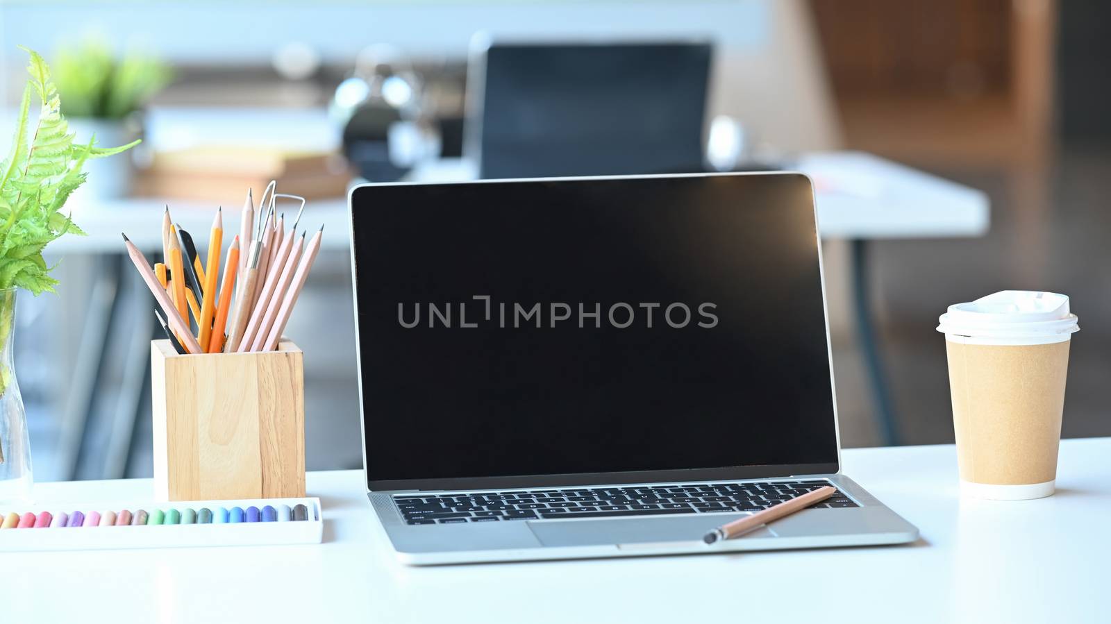 Laptop of black blank screen ,pencil holder, potted plant, coffee cup on the work desk.