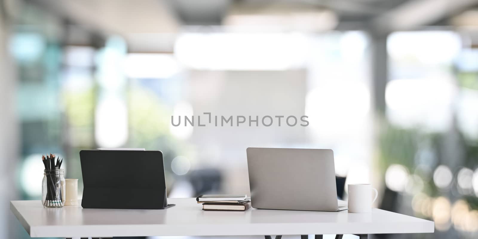 Office desk workspace with laptop, tablet and office supplies on white table in modern office.