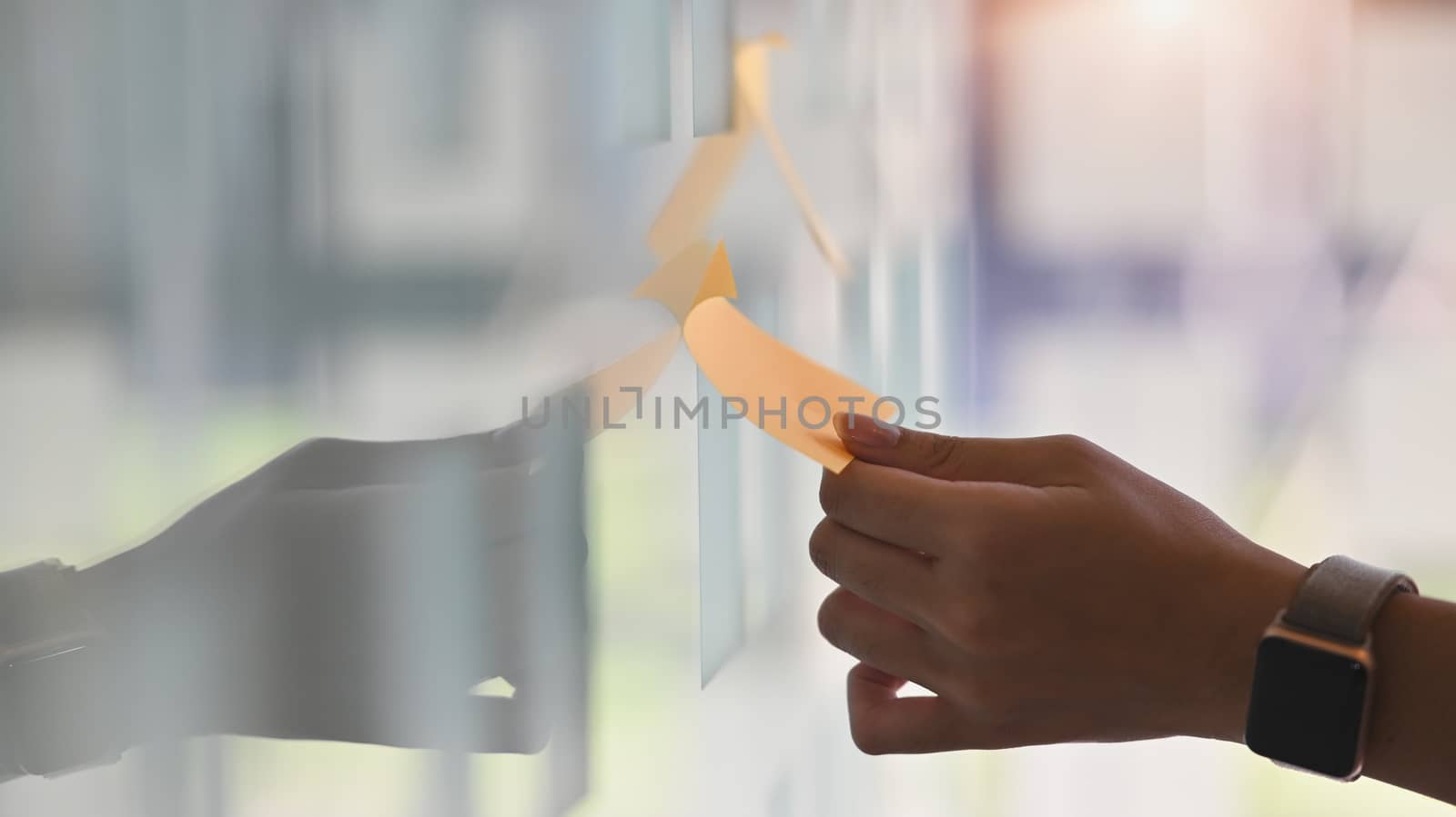 Side shot hands of young business man while sticky post it on glass. Meeting and sharing idea concept. Reminder schedule board.